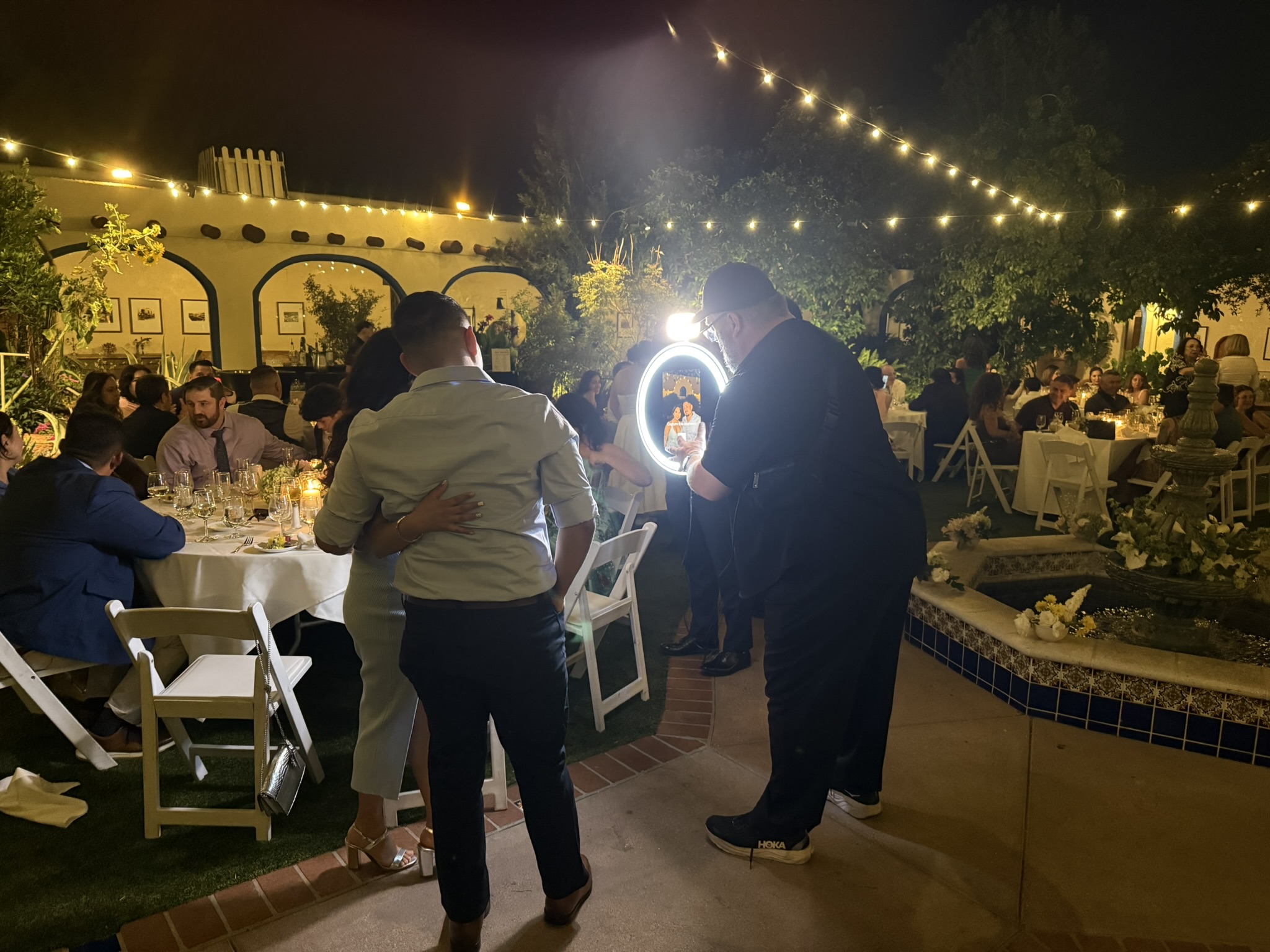 Operator using roaming portable photo booth at outdoor garden event with string lights, Tucson AZ